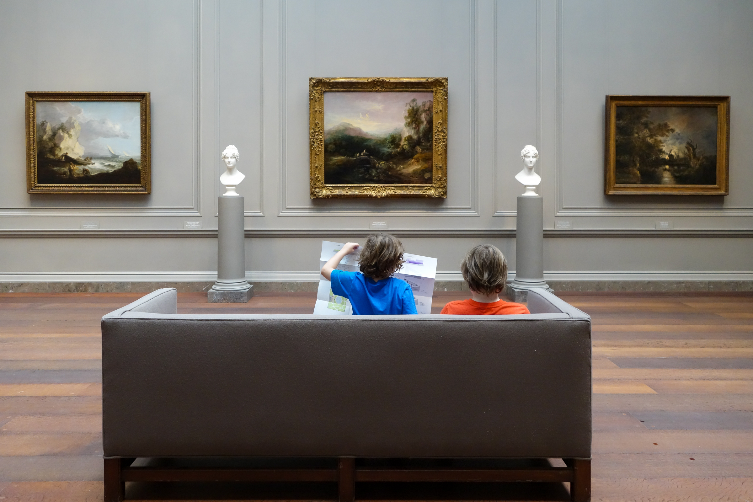 Two boys sitting on a couch looking at museum art