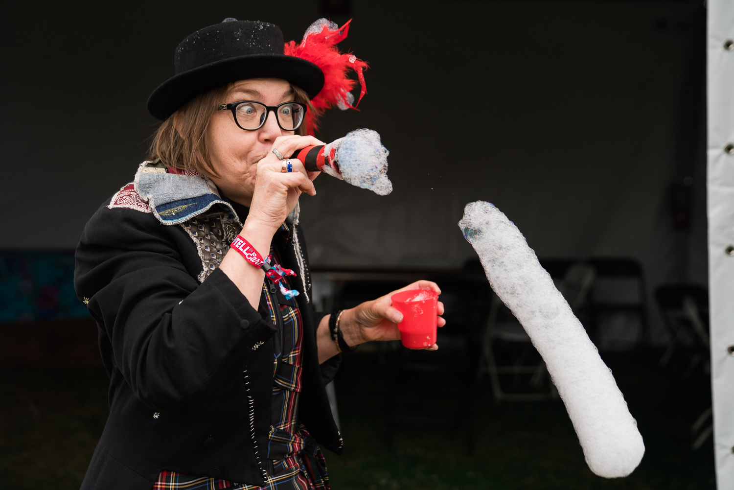 Woman in vintage dress wearing a black hat with a red feather crosses eyes while blowing bubbles.